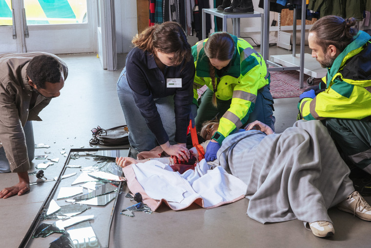 Kvinna och ambulanspersonal stoppar en bl&ouml;dning p&aring; en person.